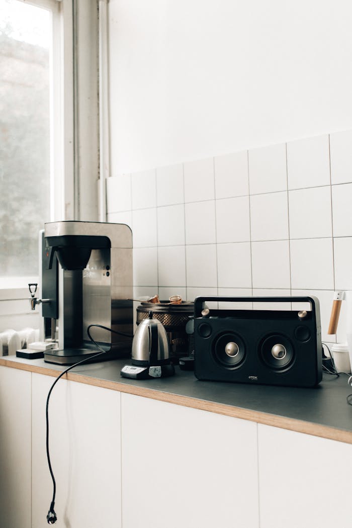 Clean minimalist kitchen setup with coffee maker and audio speaker on countertop.
